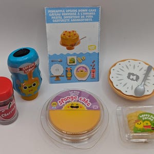 Peut inclure: Un ensemble d'aliments miniatures, comprenant un gâteau renversé à l'ananas, un gâteau éponge, une bouteille de sirop doré, un récipient de cerises et une assiette avec une cuillère. Les articles sont tous dans un style lumineux et coloré et sont parfaits pour une collection d'aliments miniatures.