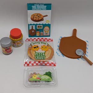 Peut inclure: Un ensemble de fournitures miniatures pour faire des pizzas, comprenant une croûte à pizza, des flocons de piment rouge, un pot de sauce, une pelle à pizza et un coupe-pizza. L'emballage comprend les mots "Sunny Bros. Pizza Crust" et "Veggie Pizza".