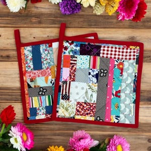 Könnte beinhalten: Zwei rote, gesteppte Topflappen mit einem Patchwork-Muster aus bunten Stoffquadraten. Die Topflappen sind aus Baumwollstoff gefertigt und eignen sich perfekt zum Schutz der Hände vor heißen Oberflächen.