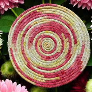 May include: A round, woven coaster with a pink and yellow spiral pattern. The coaster is made of fabric scraps and is perfect for adding a touch of handmade charm to your home decor.
