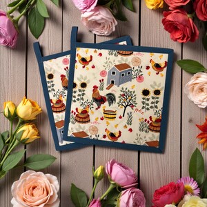 May include: Two square pot holders with a farm-themed pattern featuring chickens, sunflowers, and a small barn. The pot holders have a cream background with a navy blue border and hanging loop. The image is surrounded by colorful roses.