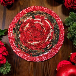 Può includere: Un sottopentola rotondo in tessuto rosso con un design a spirale. Il sottopentola presenta motivi floreali rossi e foglie verdi. Lo sfondo include rose rosse, ornamenti e una superficie in legno, creando un tema festivo natalizio.