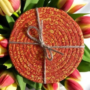 May include: Set of four round woven coasters in orange and yellow with a rope tied around them. The coasters are surrounded by yellow and red tulips.