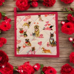 May include: A pink and white quilted hot pad with a red border. The hot pad features a pattern of dogs with hearts and balloons.