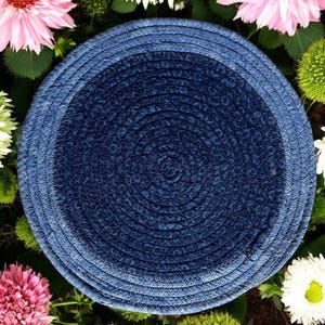 May include: A blue and white woven round placemat with a circular design. The placemat is surrounded by flowers.
