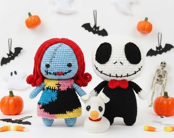 May include: Three crocheted dolls featuring a blue-skinned character with red yarn hair, a white-headed character in a black suit with a red bow tie, and a small white dog with a red collar, all displayed with miniature Halloween decorations.