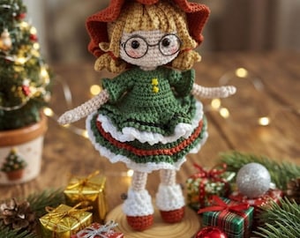 May include: A crocheted doll with blonde hair, wearing a wide-brimmed rust-colored hat, round black glasses, and a green dress with white ruffled trim. The doll has light skin, beige arms and legs, and wears small rust-colored shoes.