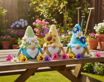 May include: Three crocheted gnomes with pointed hats, each featuring a white beard and a round nose. The left gnome has a green hat with white daisies, the center has a yellow hat with a sunflower, and the right has a blue hat with blue and white flowers.