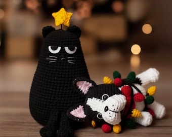 May include: A black crocheted cat figure with a yellow star on its head sits next to a black and white crocheted dog figure wrapped in a string of colorful crocheted Christmas lights, including red, yellow, and green bulb shapes.