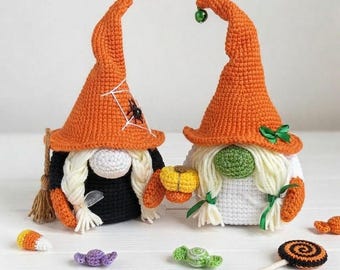 May include: Two crocheted gnomes with orange pointed hats. The left gnome wears a black outfit with a spiderweb design and holds a broom. The right gnome wears a white outfit, holds a yellow pumpkin, and has a green bell on its hat tip.