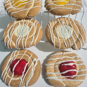 May include: Six pastry swirls with different fillings. Two have a yellow filling, two have a white filling, and two have a red filling. All are topped with white icing.