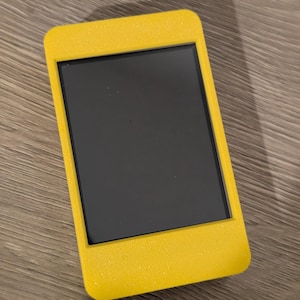 May include: A rectangular, yellow electronic device with a black screen. The device has rounded corners and a textured, glittery finish. The screen is black and appears to be off. The device is likely a handheld electronic gadget.