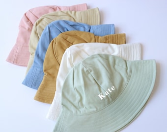 May include: A stack of six colorful bucket hats, with the top hat being a light green color and the text "Kate" embroidered on the front. The hats are made of a soft, cotton fabric.