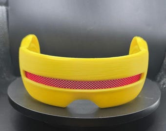 May include: A bright yellow visor with a horizontal cutout across the center. The cutout features a textured, metallic red insert with a fine diamond-patterned grid. The visor has a curved, wrap-around shape with smooth, solid yellow edges.