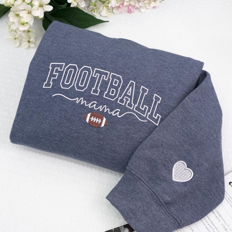 Custom embroidered Football Mama sweatshirt in Heather Dark Navy, featuring varsity lettering with football design on chest and white heart embroidery on sleeve. Soft cotton-poly blend for cozy everyday wear. Perfect game day outfit, thoughtful gift for football moms, or team spirit apparel. Handmade embroidery adds a premium, one-of-a-kind touch. Available in multiple sizes and colors.