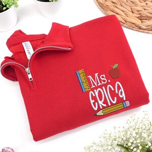 Custom embroidered red quarter-zip sweatshirt with “Ms. Erica” and cute apple, pencil, and ruler design — personalized teacher sweatshirt, perfect for back-to-school, thoughtful teacher appreciation gift, or cozy everyday classroom wear.