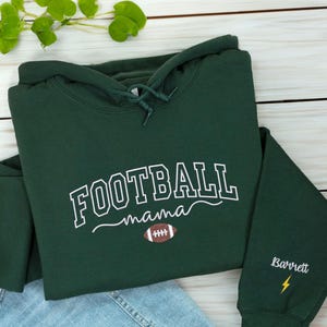 Custom embroidered Football Mama hoodie in Forest Green, featuring varsity lettering with football design on chest and personalized sleeve with name 'Barrett' and yellow lightning bolt. Cozy cotton-poly blend for warmth and durability. Perfect gift for football moms, game day outfits, or showing team spirit. Handmade embroidery adds a premium, one-of-a-kind touch. Available in multiple colors and sizes