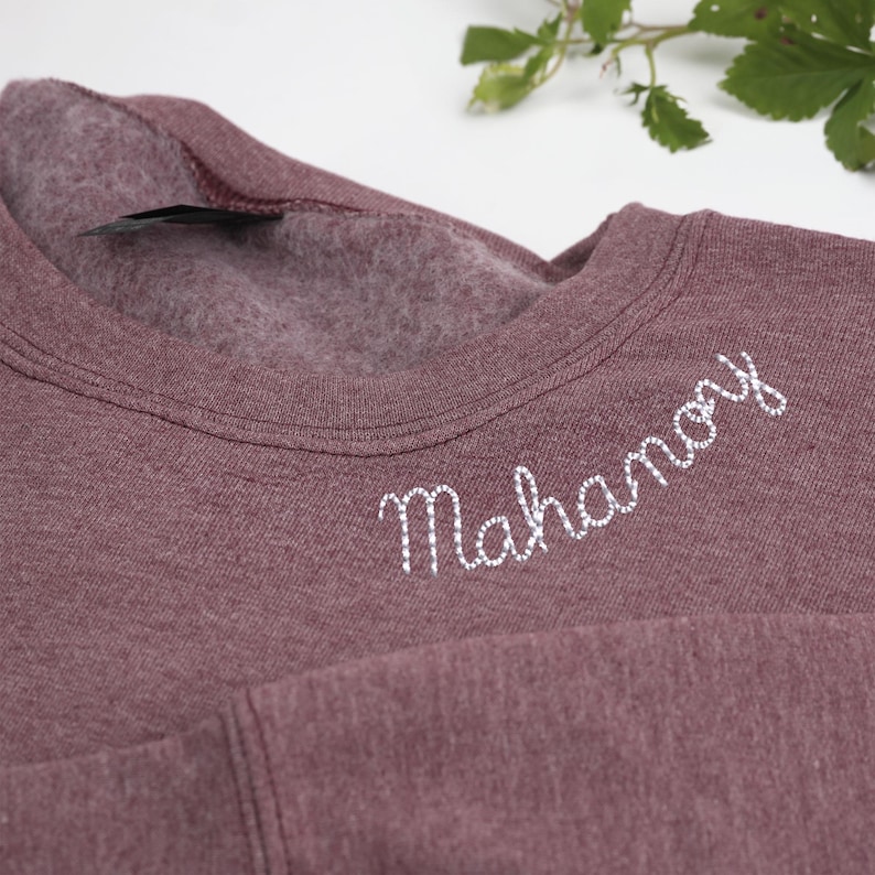 Heather dark maroon Gildan sweatshirt with custom embroidered text 'Mahanoy' in white cursive on the collar. Soft, cozy unisex crewneck perfect for personalized school spirit wear, sports team apparel, or thoughtful custom gifts. Ideal for students, alumni, and fans looking for unique embroidered clothing for game day, casual wear, or special occasions