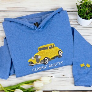 Heather royal embroidered hoodie with detailed yellow vintage car and text “Classic Beauty.” A timeless embroidered sweatshirt for classic car lovers and collectors, handmade with care.