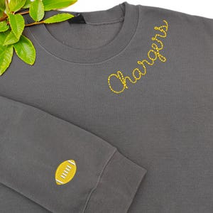 Charcoal sweatshirt with “Chargers” embroidered in yellow script on the chest and a small yellow football with white stitching detail on the sleeve. Made from soft, cozy fabric, perfect for football fans and team spirit wear. Ideal for game days, school events, or casual outings, showcasing sporty style and team pride.