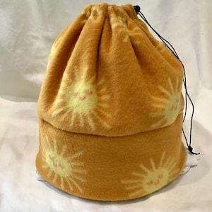 May include: A golden yellow fleece drawstring bag with a repeating sunburst pattern in a lighter yellow. The bag has a black drawstring closure. The text "SewAndSoByDona" is printed at the bottom of the image.