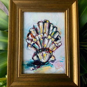 May include: A framed oil painting of a seashell. The artwork features a colorful seashell with white, yellow, red, and blue hues. The painting is set against a white and light blue background and is enclosed in a gold-colored frame.