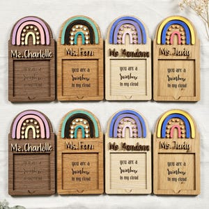 May include: Eight wooden rainbow-shaped plaques with a cutout space for a photo. Each plaque has a different color rainbow and the text "You are a rainbow in my cloud" and a teacher's name: Ms. Charlotte, Ms. Fern, Ms. Pandora, and Ms. Judy.