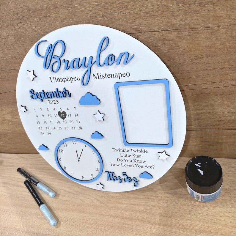 May include: A white wooden decorative plaque with blue accents, featuring the name "Braylon", a calendar for September 2025, a clock, and a photo frame. The plaque also includes the text "Twinkle Twinkle Little Star".