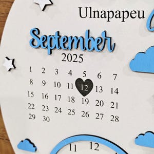 May include: A white wooden calendar with the month "September" in blue script, the year "2025", and a calendar grid. The 12th day is marked with a black heart. Decorative stars and clouds are also present.