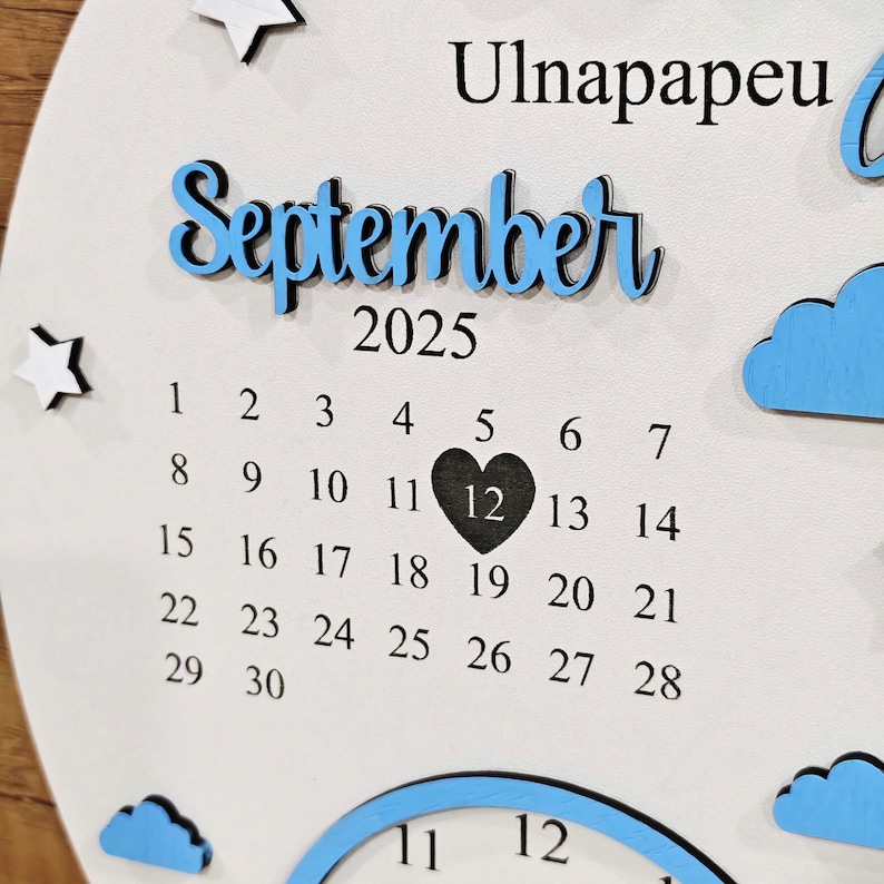 May include: A white wooden calendar with the month "September" in blue script, the year "2025", and a calendar grid. The 12th day is marked with a black heart. Decorative stars and clouds are also present.