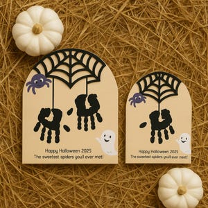 Pode incluir: Duas decorações de Halloween com um design de teia de aranha, aranhas de pegadas de mãos e um fantasma. O texto diz "Happy Halloween 2025" e "The sweetest spiders you'll ever met!" Duas abóboras brancas também estão presentes.