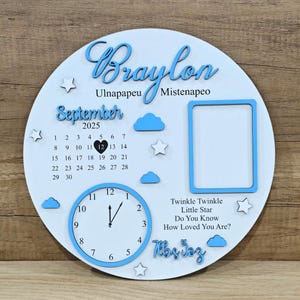 May include: A white wooden circular plaque with blue accents. The plaque features the name "Braylon", a calendar for September 2025, a clock, and a photo frame. Decorative clouds and stars are also included. The text "Twinkle Twinkle Little Star" is also present.
