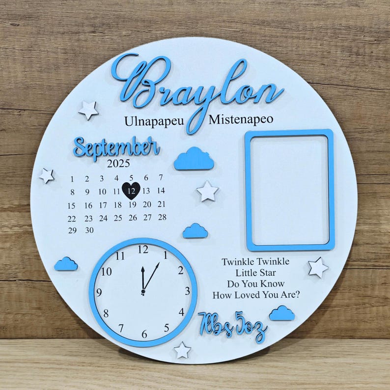 May include: A white wooden circular plaque with blue accents. The plaque features the name "Braylon", a calendar for September 2025, a clock, and a photo frame. Decorative clouds and stars are also included. The text "Twinkle Twinkle Little Star" is also present.