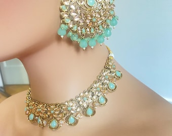 May include: A gold necklace and earrings set with light blue and clear stones. The necklace is a choker style with a delicate design. The earrings are large and dangle.