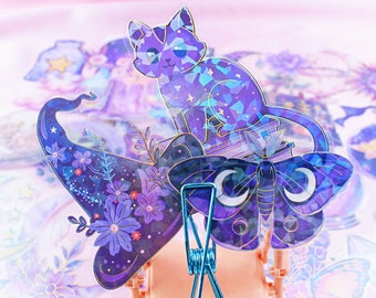 May include: A set of holographic stickers featuring a purple cat, a witch's hat, and a moth. The stickers have a sparkly, iridescent finish and are perfect for adding a touch of whimsy to your crafts or journals.