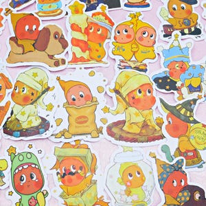 Puede incluir: Una colección de pegatinas coloridas con personajes de dibujos animados en varios disfraces y poses. Las pegatinas muestran personajes con piel naranja, que llevan sombreros, pijamas y otros atuendos. Algunas pegatinas incluyen texto y están rodeadas de estrellas.