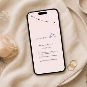 May include: A smartphone displaying a digital save the date announcement on a pale pink background with a string of fairy lights graphic. The text reads: save our date, LAURA & MATHIAS, 17.07.2027, and additional German wedding invitation details.