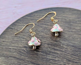 May include: A pair of gold-toned dangle earrings featuring small mushroom charms. Each charm has a pale mint green cap decorated with raised, glossy light pink polka dots and a gold-toned stem, suspended from simple gold-toned ear wires.