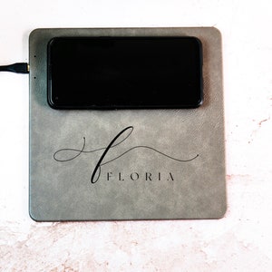 May include: A gray leather charging pad with the word "FLORIDA" printed in black cursive script. A black smartphone is charging on the pad.