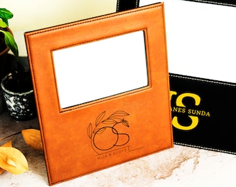 May include: Two leather picture frames with a white mat and a stitched border. The frame on the left has a personalized design with the initials "OS" and the names "OLIA & SCOTT". The frame on the right has the initials "JS" and the name "JAMES SUNDA".