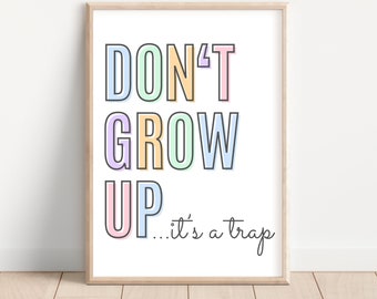 May include: A framed print with the text "DON'T GROW UP...it's a trap" in colorful letters. The letters are outlined in black and have a pastel color scheme.