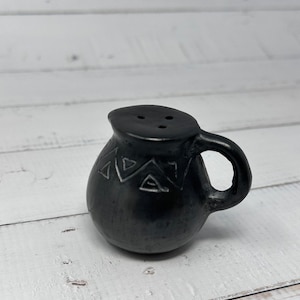 K&ouml;nnte beinhalten: Ein kleiner schwarzer Keramik Krug mit Henkel und geometrischem Muster. Der Krug hat drei L&ouml;cher oben.
