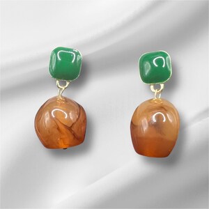 May include: A pair of dangle earrings with a green square top and a brown, marbled, teardrop-shaped bottom.