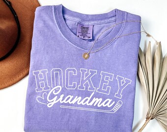 May include: A purple t-shirt with the text "Hockey Grandma" in white with a hockey stick graphic. The shirt is made of a soft, comfortable material.