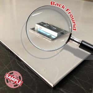 Może przedstawiać: Zbliżenie na metalowy wspornik z lupą, kt&oacute;ra pokazuje szczeg&oacute;ły. Wspornik jest srebrny i ma prostokątny kształt. Tekst "Back Fround" jest napisany na czerwono na lupie.