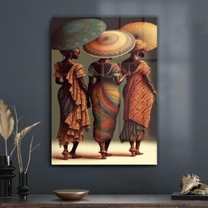 May include: Three women in colourful dresses and head wraps walk together, each holding a traditional umbrella. The umbrellas are decorated with intricate patterns and colours. The women are wearing gold jewellery and have dark skin.