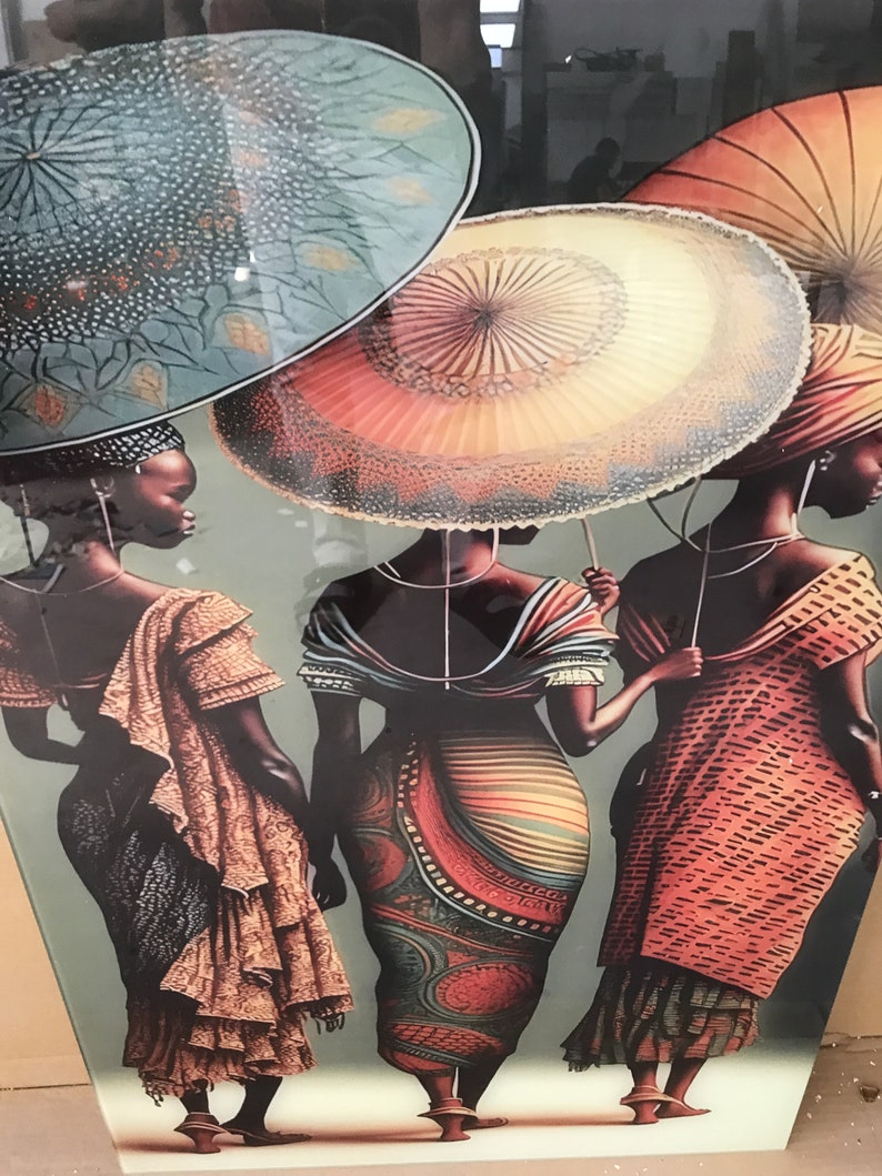 May include: Three women wearing colourful patterned dresses and head wraps stand under large, patterned umbrellas. The umbrellas are a teal blue, a light orange with a white lace trim, and a red and orange umbrella.