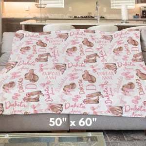 a personalized western baby girl blanket featuring pink coquette bows on cowgirl hats and boots is draped across a living room couch. the size is 50" x 60"