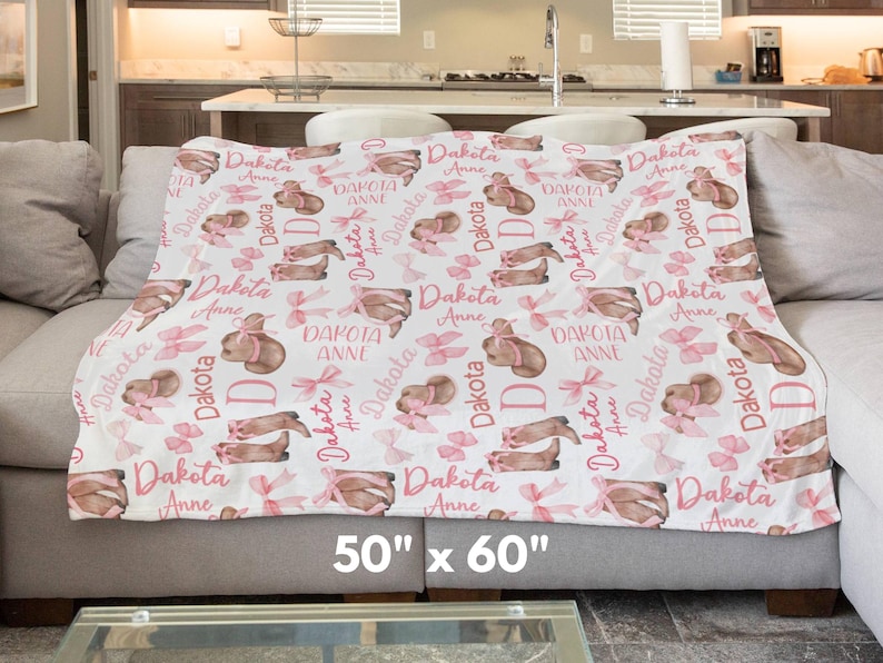 a personalized western baby girl blanket featuring pink coquette bows on cowgirl hats and boots is draped across a living room couch. the size is 50" x 60"