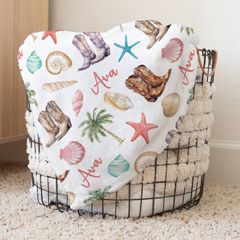 Custom name coastal cowgirl beach pattern blanket. Blanket features jeweled cowgirl boots, beach shells in peaches, turquoise, and cream colors, and personalized girl's name in a salmon color.